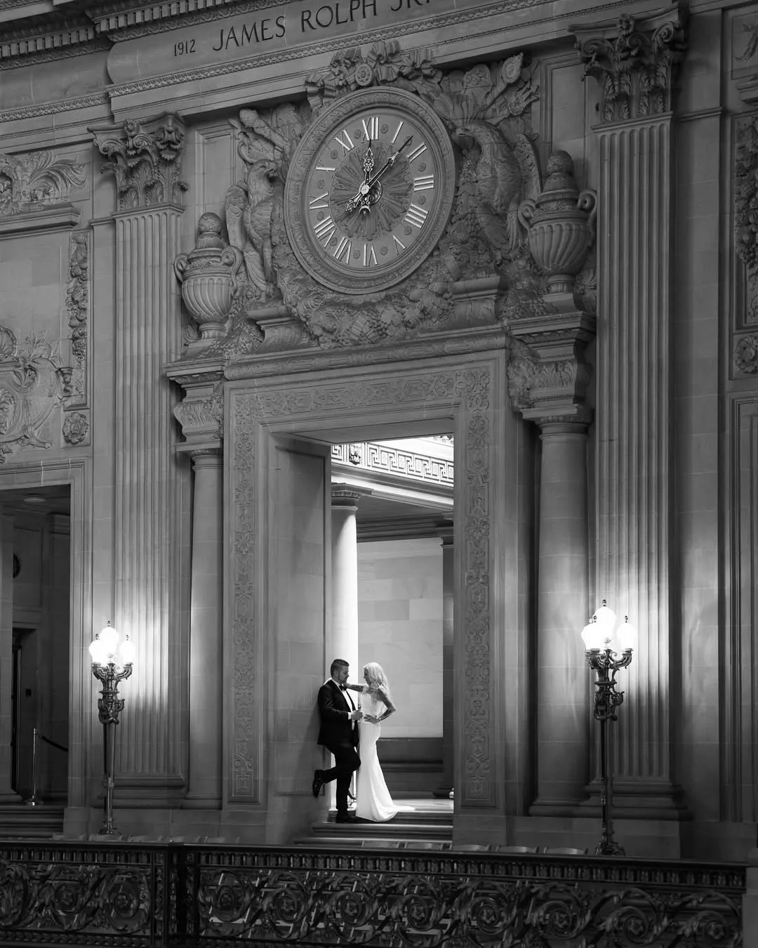 Matthew and Jacinda, Boss & Blondie, in wedding attire beneath the ornate clock at San Francisco City Hall.